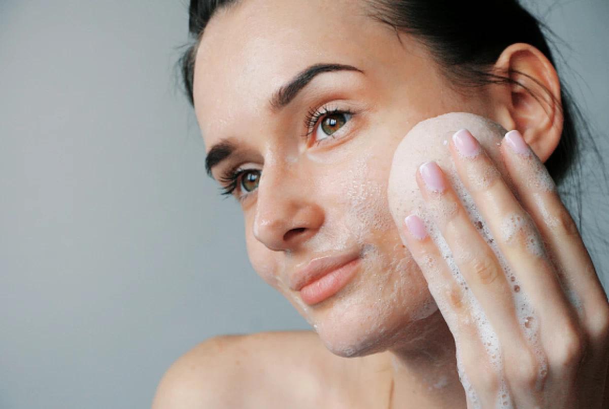 Une femme se nettoie le visage avec une mousse nettoyante végane.
