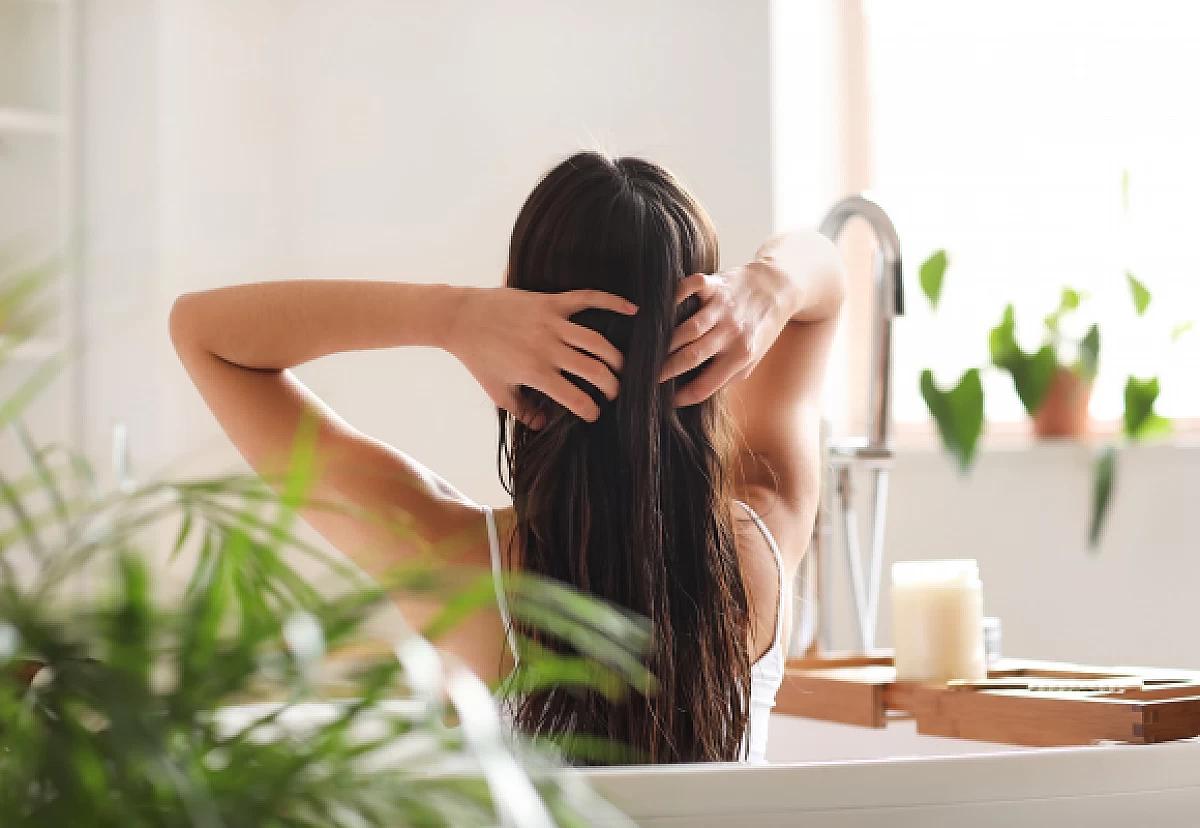 Person pflegt sich lange Haare in Badewanne